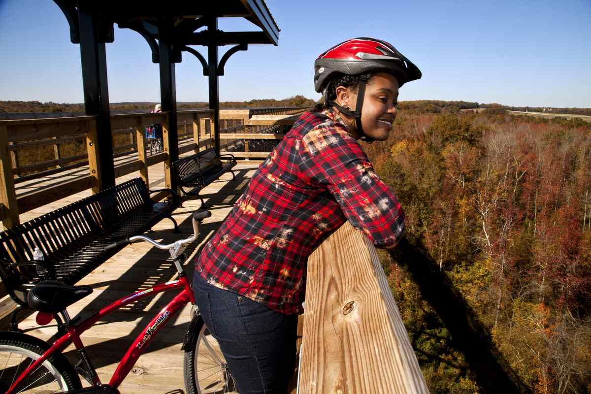 Girl in bike helmet leaning over railing of bridge