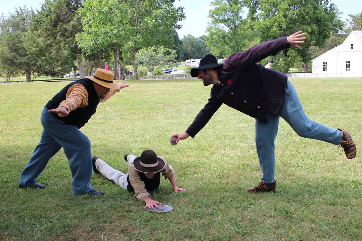 Man sliding into base while another man tries to tag him with ball, and a third man spreads arms wide