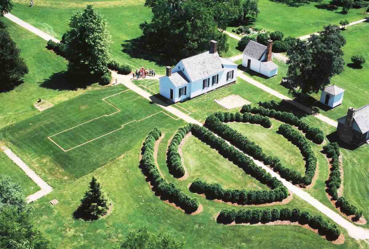 aerial view of small white house and outbuildings with shaped hedges