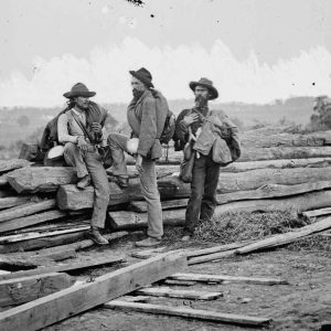 Three men standing next to pile of lumber