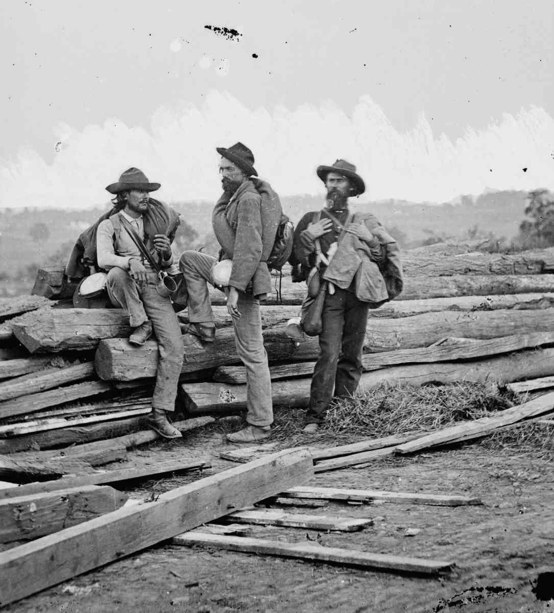 Three men standing next to pile of lumber