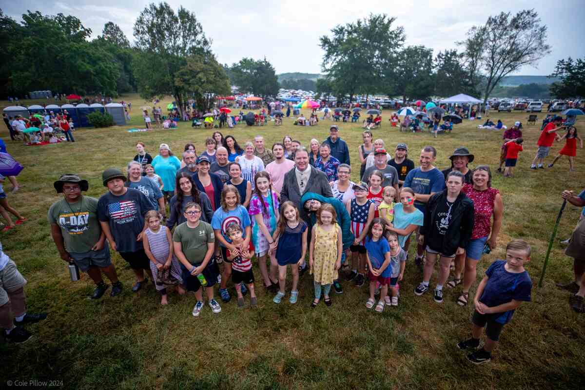 Large group of adults and children gathered in field