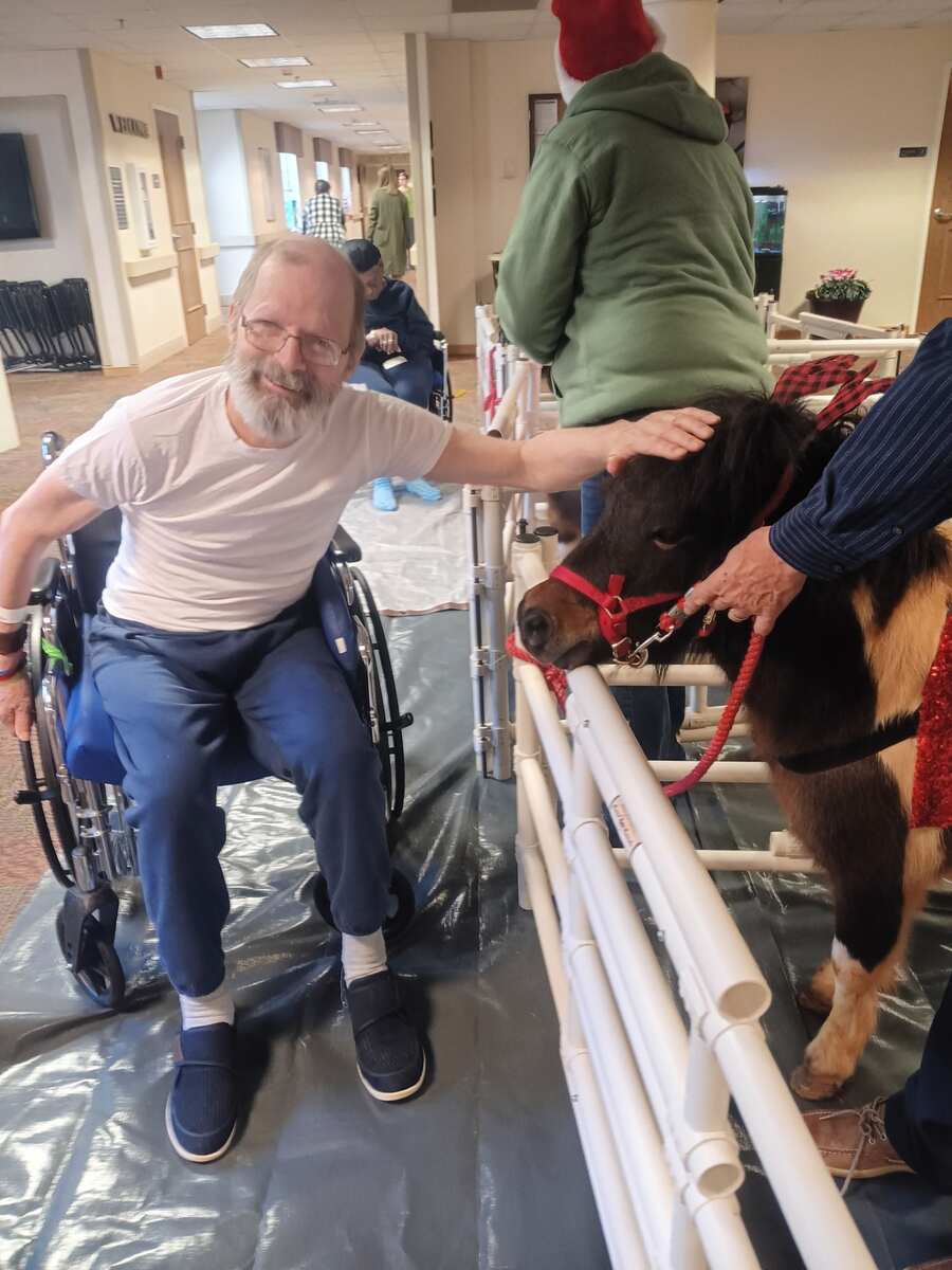 Man in wheelchair petting miniature horse