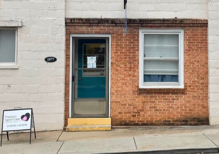 Door and sidewalk of brick building with sign for Pregnancy Support Center
