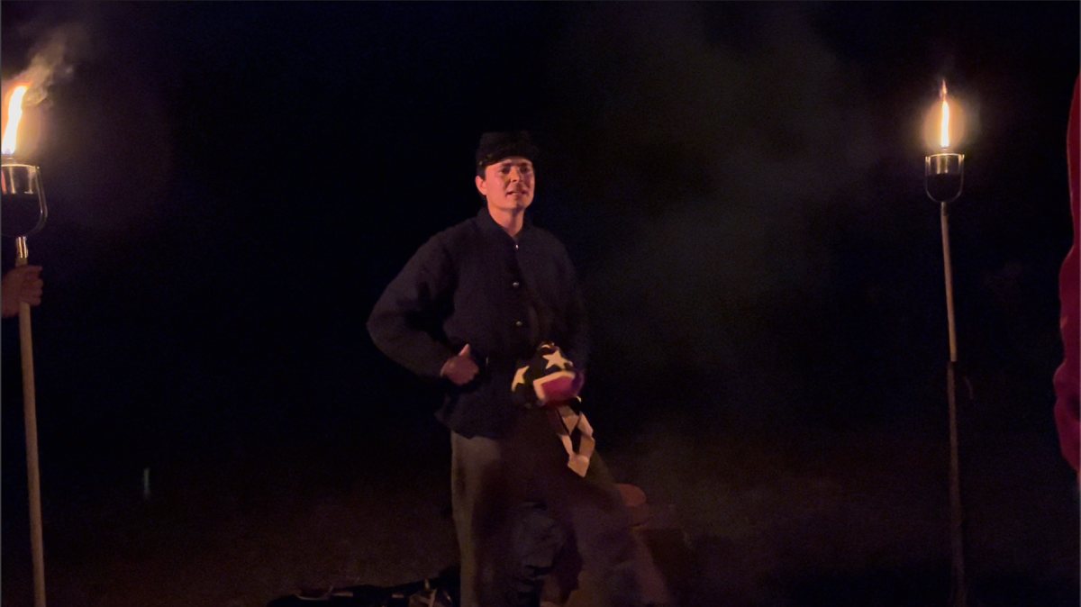 Man in confederate uniform standing in darkness with two torches