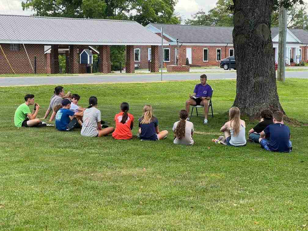 Youth sitting on grass, with man on chair reading book