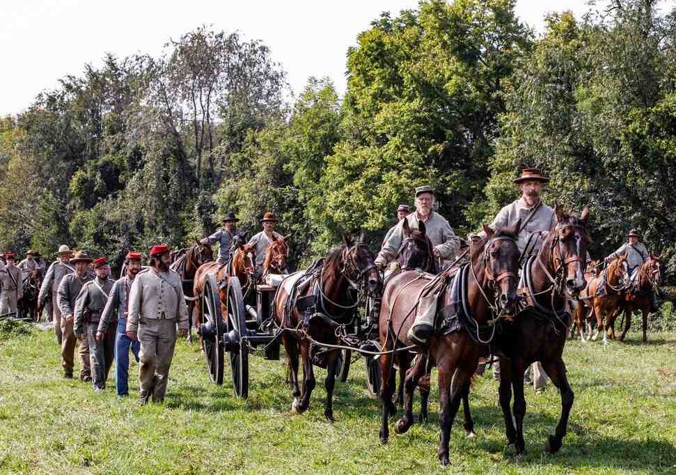 Men in Civil War Uniforms walking and riding horses beside horse drawn wagon