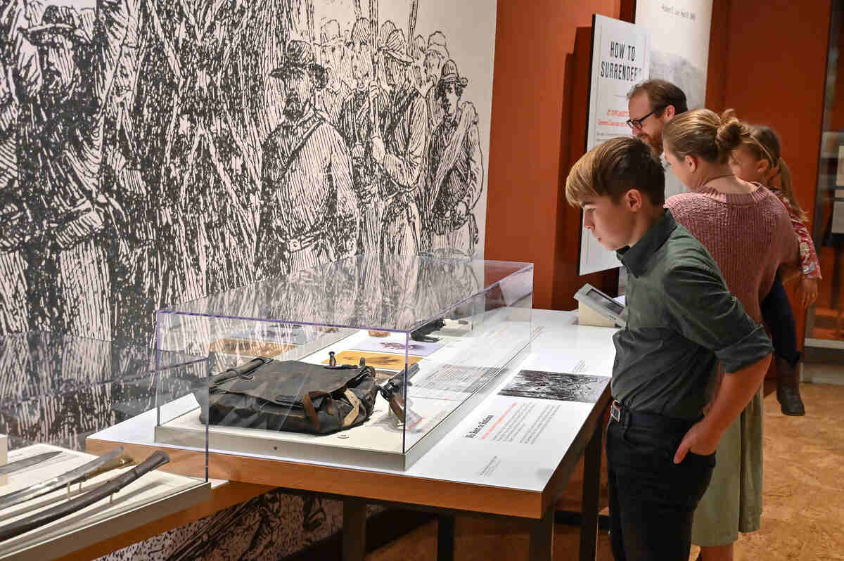 Display at the American Civil Warm Museum with a young man reading the information in front of a gun and case.