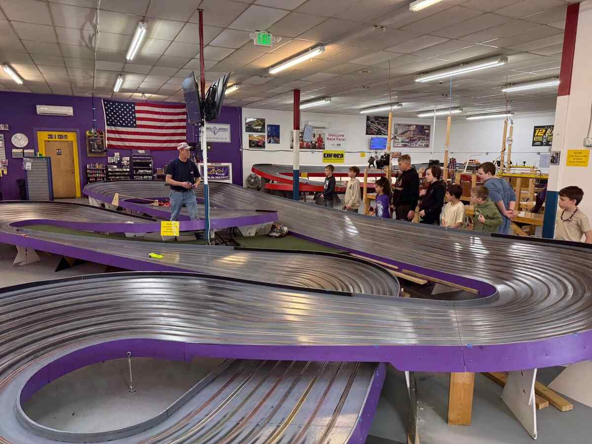 Toy racecar track with a man talking with several children