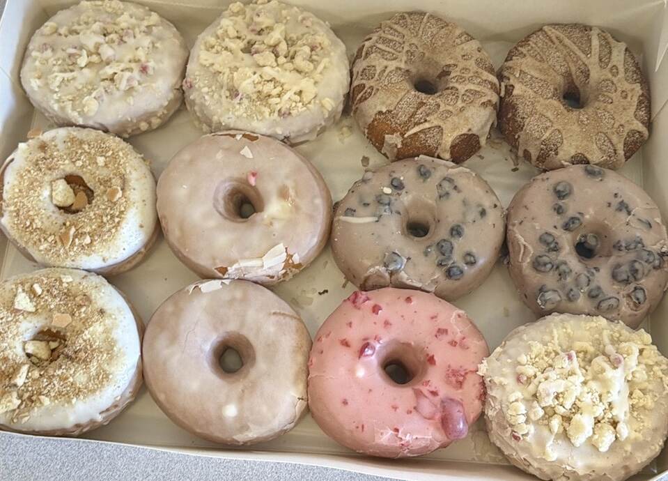 Box of dozen donuts with a variety of toppings.