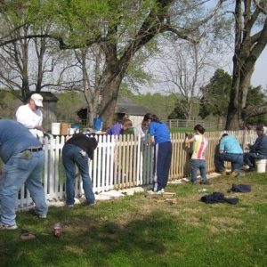 Several people scraping and repainting fence