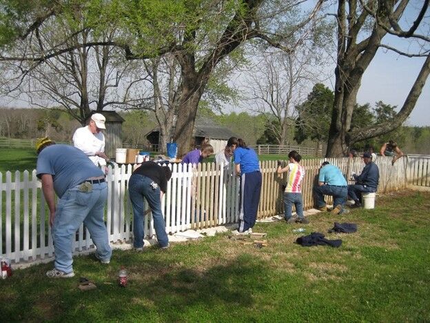 Several people scraping and repainting fence
