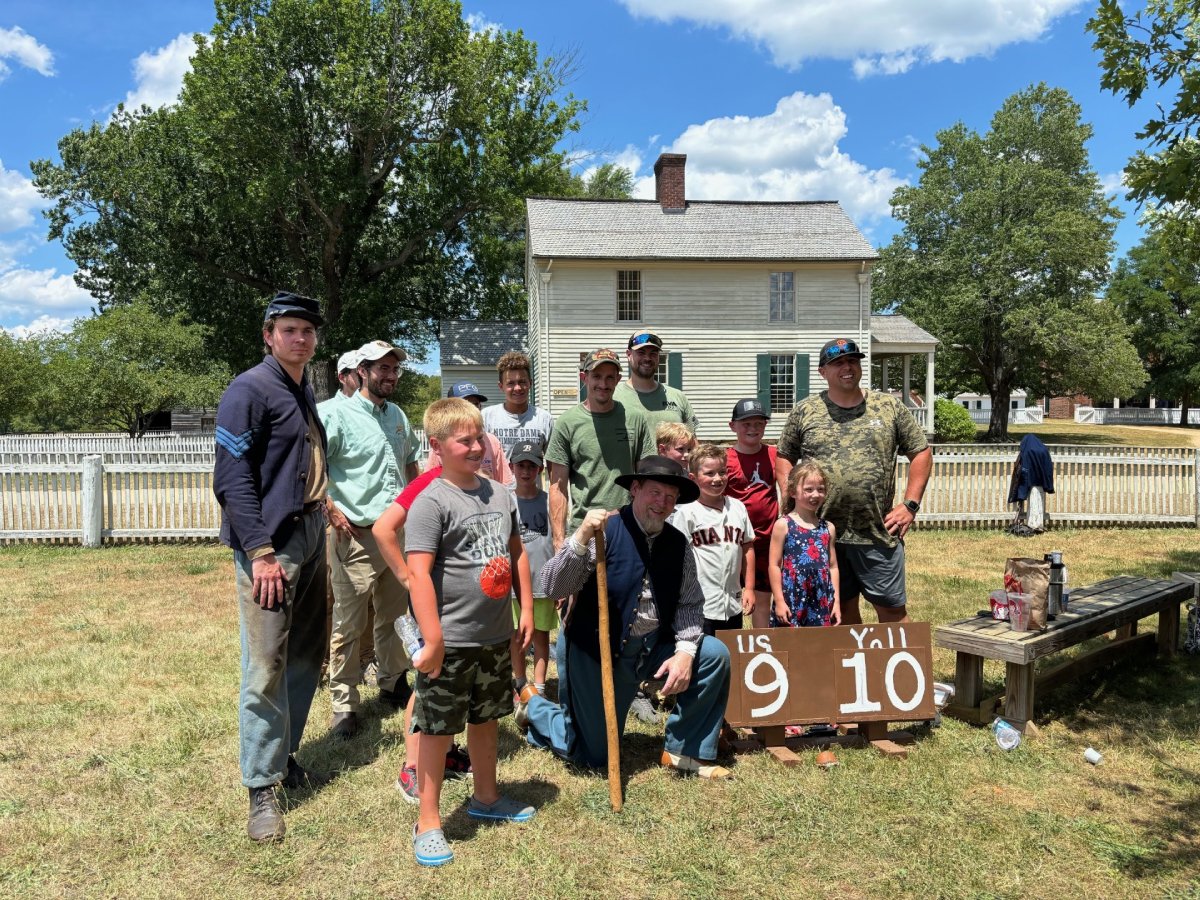 Group of people standing next to man dressed as civil war soldier, and a scoreboard with us and yall