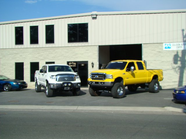 yellow and white truck in parking lot of hi end auto with building in back